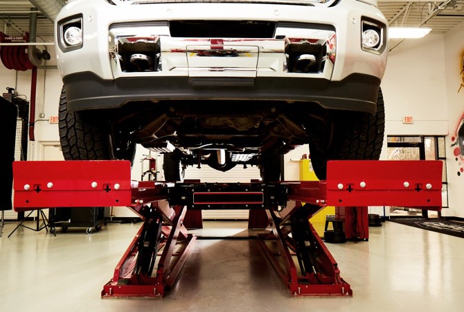 A vehicle that is lifted up into the air on a hoist in a mechanics bay.