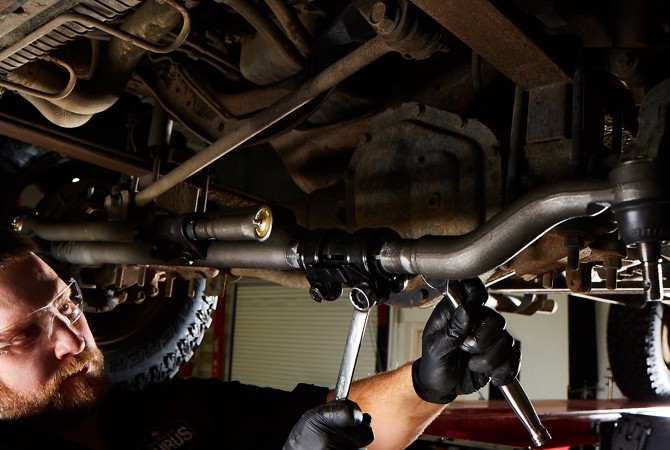 A mechanic checking over the bottom of a vehicle to ensure no damage has been done to the undercarriage.